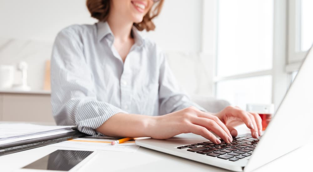 A smiling woman is researching web hosting on her laptop.