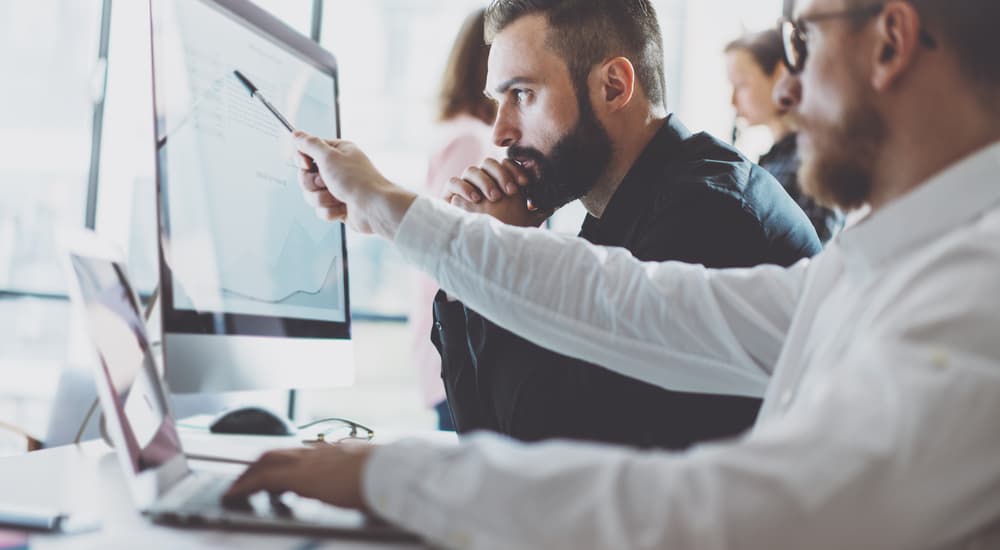 Two men in dress shirts are looking at domain registration on a computer.