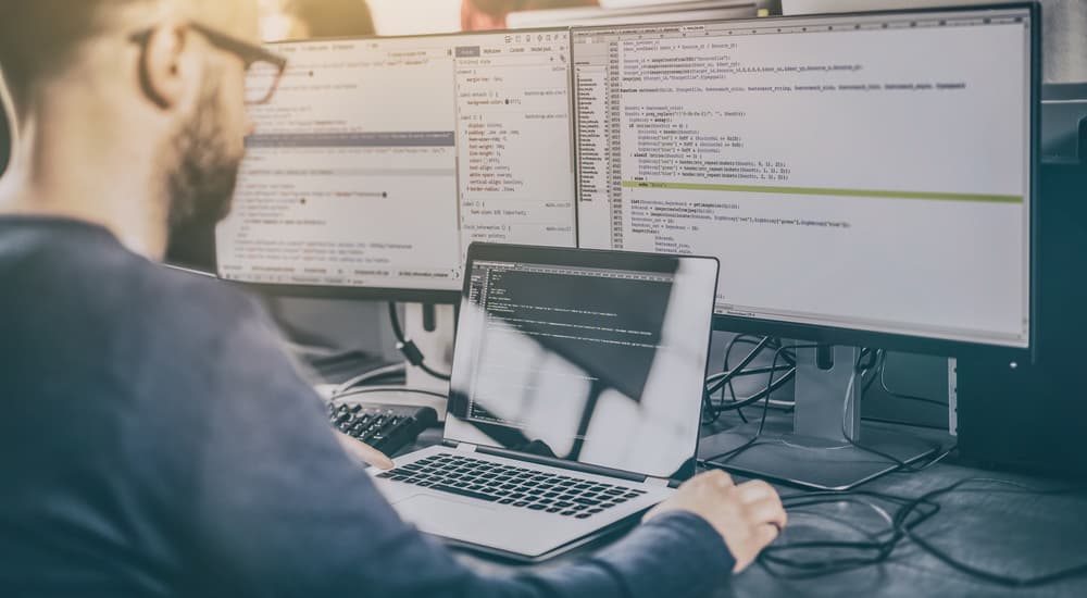 A man with two monitors and a laptop is coding a website.